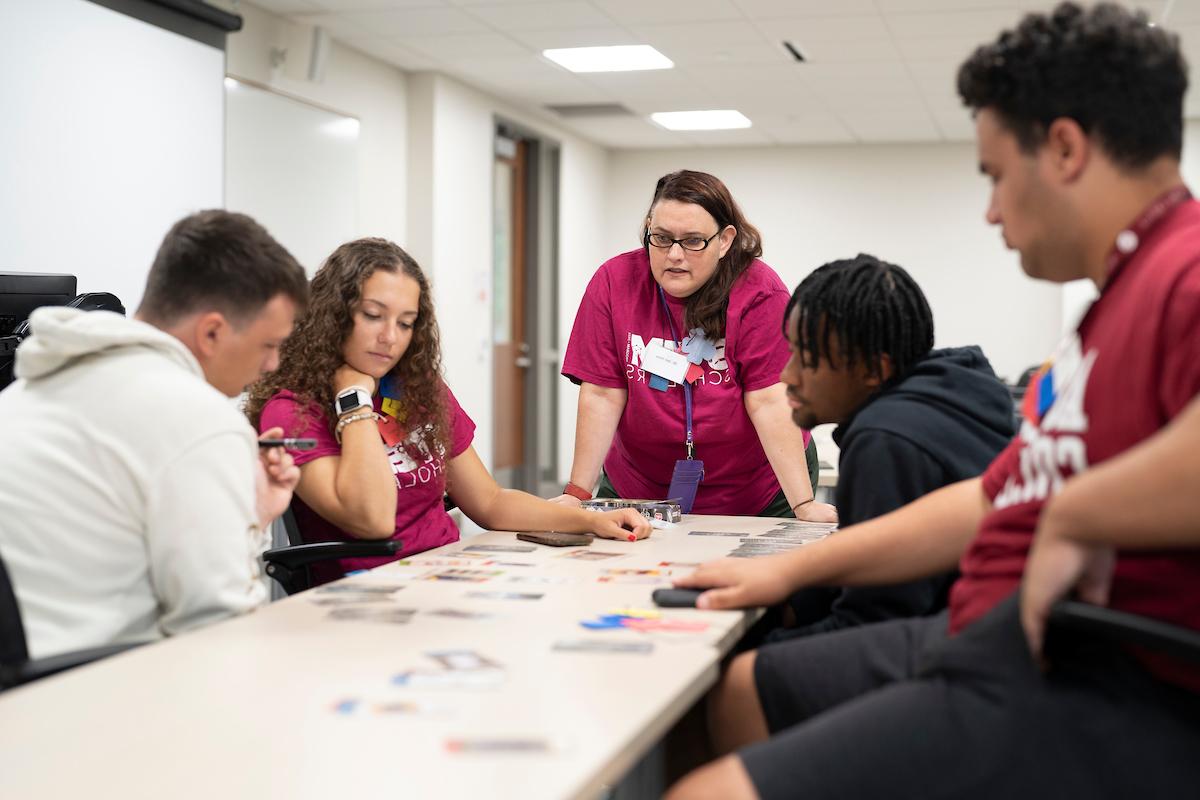 Students looking at cards on a table intently with a professor